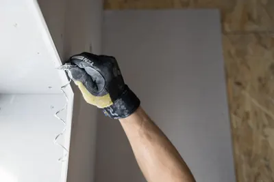 Gloved hand cutting a drywall panel with a knife