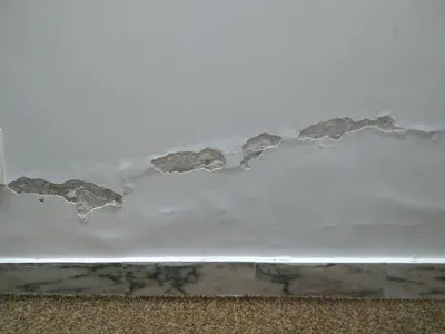 White wall with bubbling and peeling paint above a stone baseboard