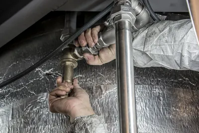 Plumber hands tightening a pipe fitting wrapped with foil insulation
